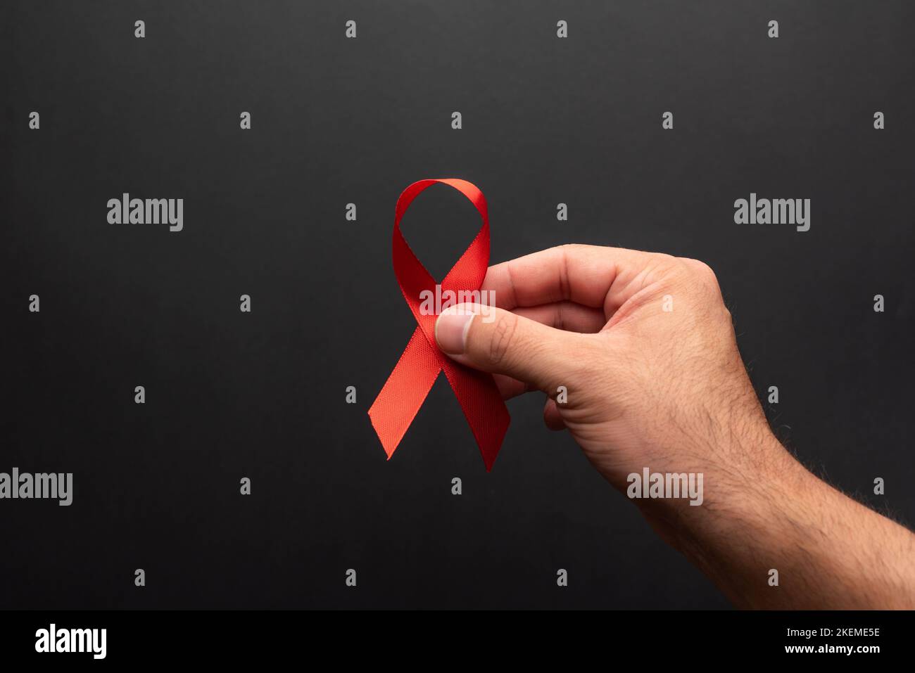 A man's hand holding a red ribbon in support of World AIDS Day on a black background. december 1, hiv day Stock Photo