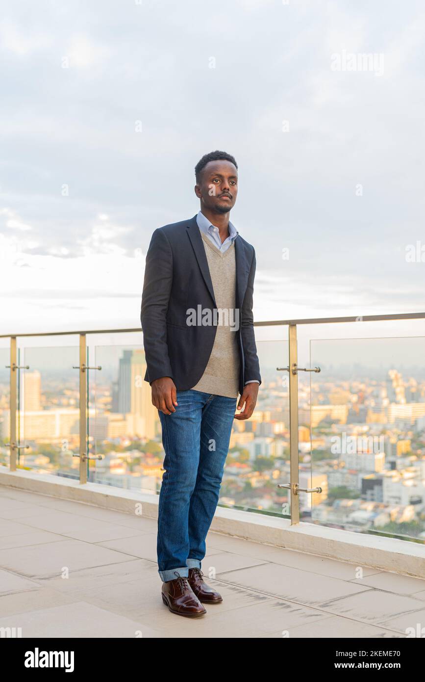 Portrait of handsome black African businessman wearing suit full length ...