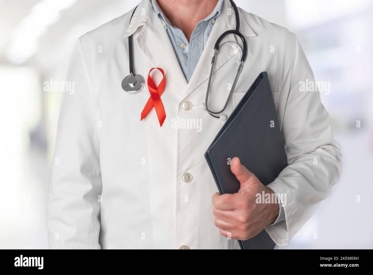 Doctor holding a folder with medical reports and wearing a red ribbon on his chest, symbol of World AIDS Day. Support from health personnel to people Stock Photo