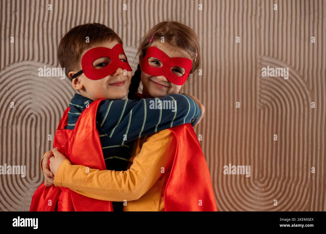 Portrait of a team of two young superheroes, brother and sister, over beige background. Superhero child. Super hero kid playing at home. Idea, freedom Stock Photo