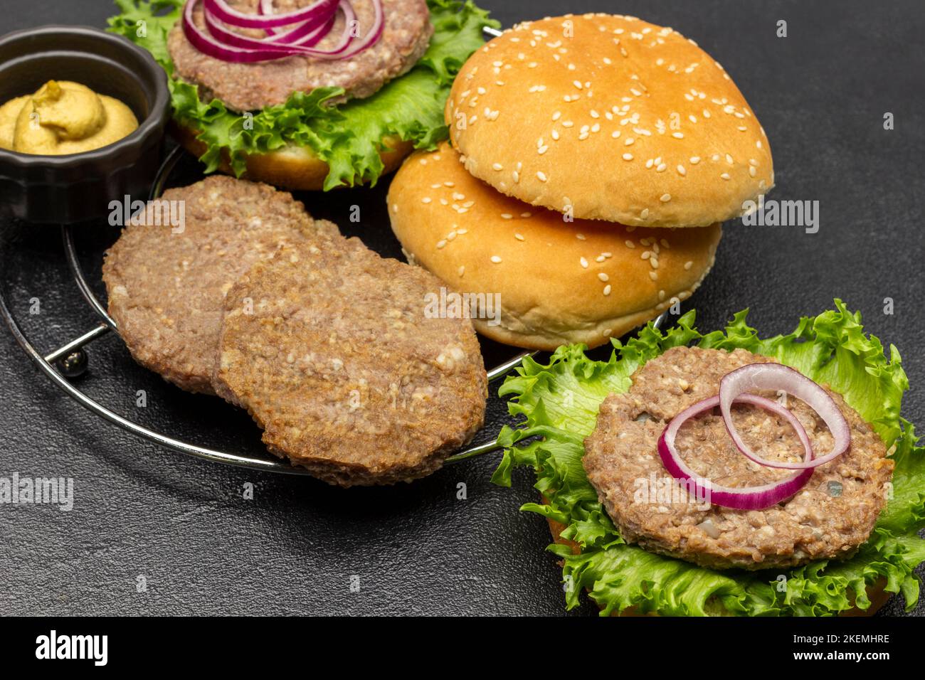 Round buns, beef burger with greens and chopped onions. Mustard in bowl