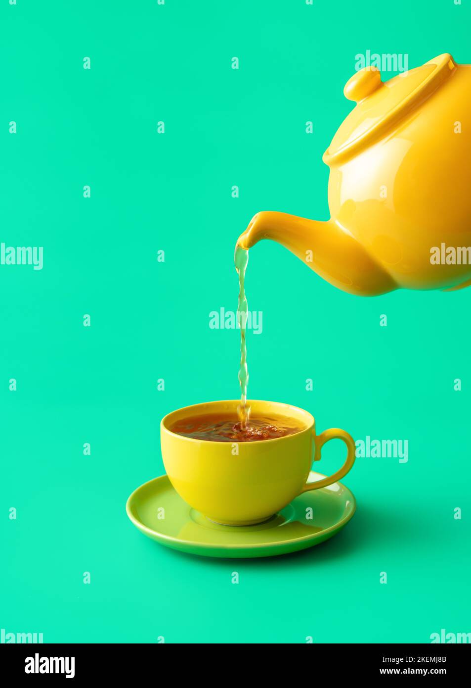 Pouring tea from a ceramic teapot in a cup, minimalist on a green table. Hot mint tea in a yellow colored cup isolated on a green background Stock Photo