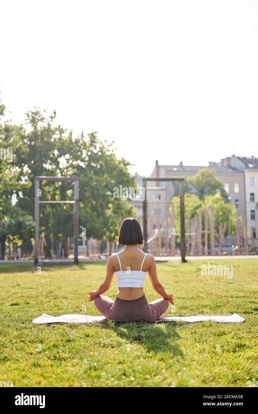 Rear view of young woman meditating in morning park, relaxing ...
