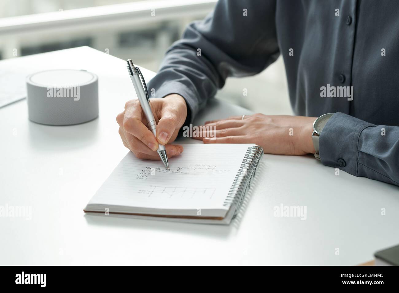 Close-up of young manager making notes in her notepad while sitting at table with smart speaker Stock Photo