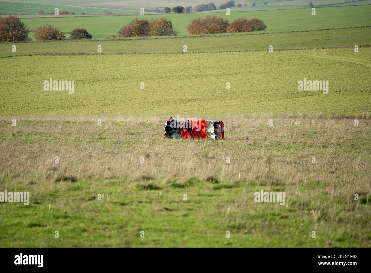 A parachutist gathering the parachute having landed in a grass meadow Stock Photo