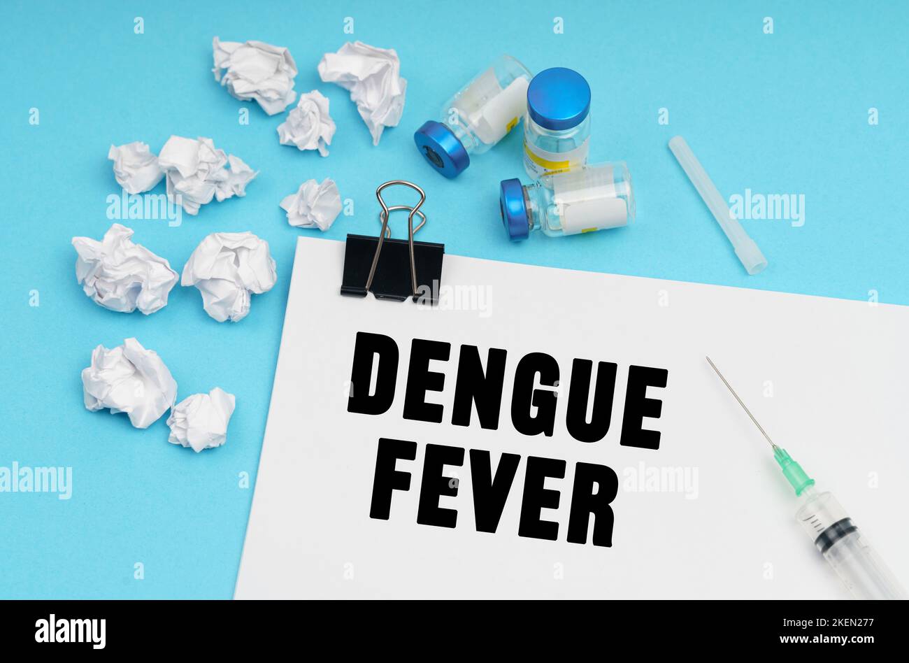 Medicine concept. On a blue background, a syringe, medicine, white crumpled pieces of paper and a sheet with the inscription - DENGUE FEVER Stock Photo