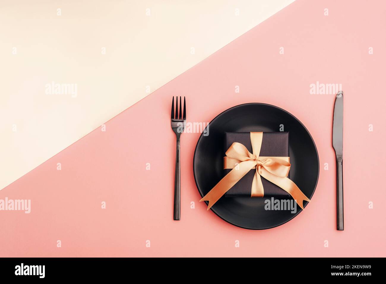 Stylish table setting, gift box, black plate, cutlery on pink and