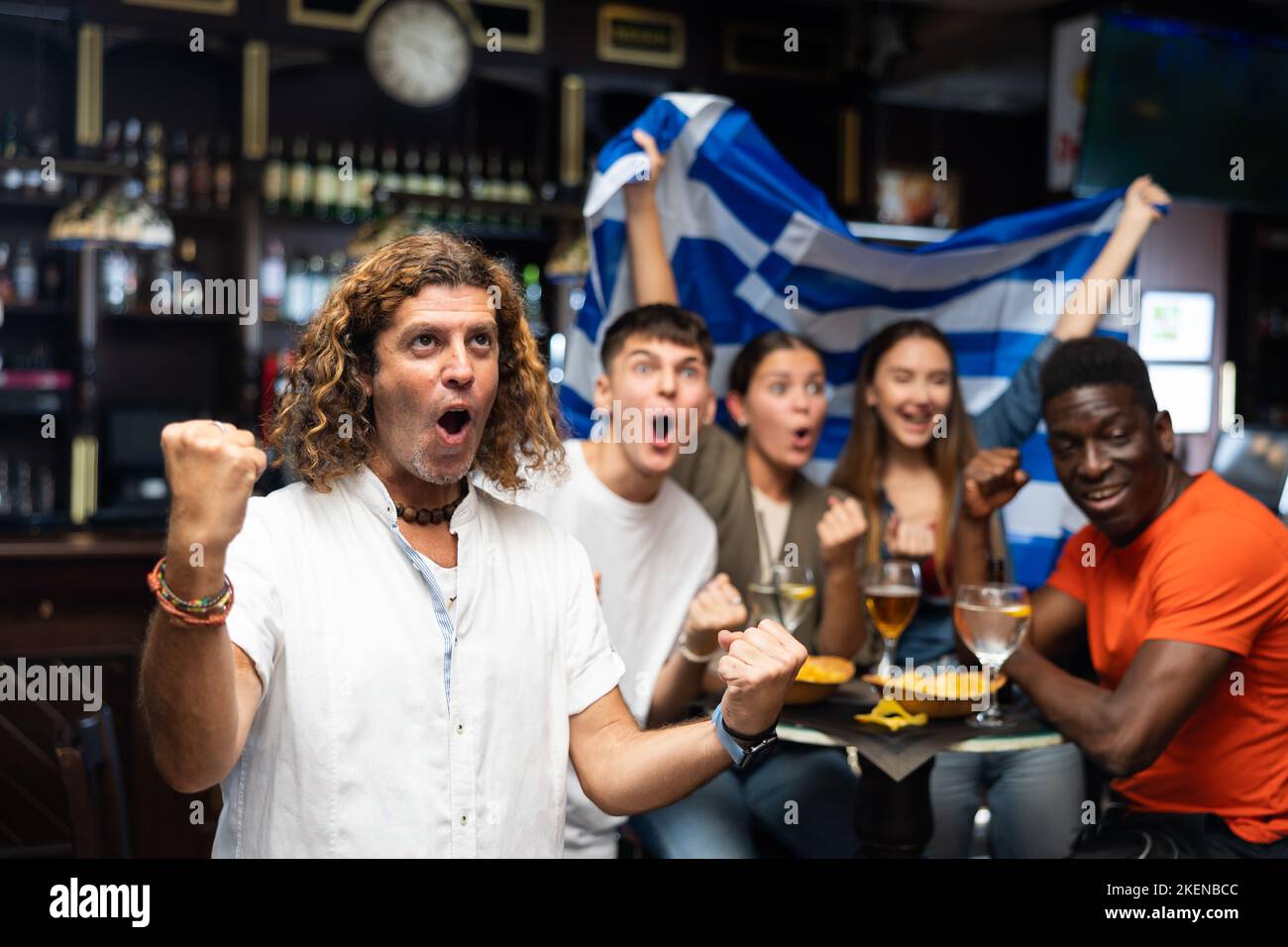 Happy multiracial sport fans with flag of Greece with pint of beer and