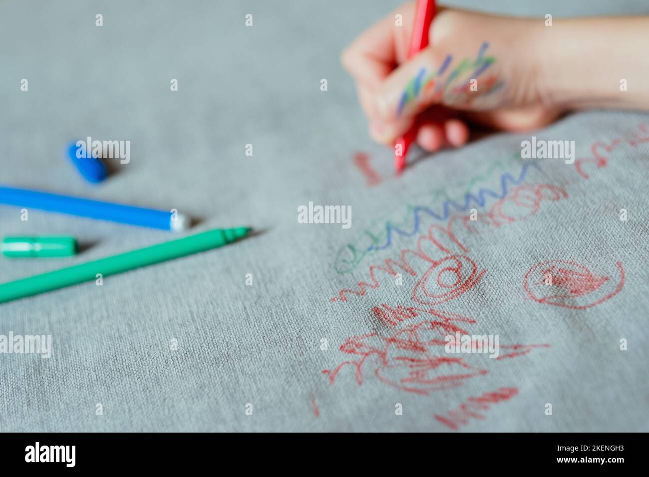 Kid freehand drawing red felttip pen on the upholstery of the couch