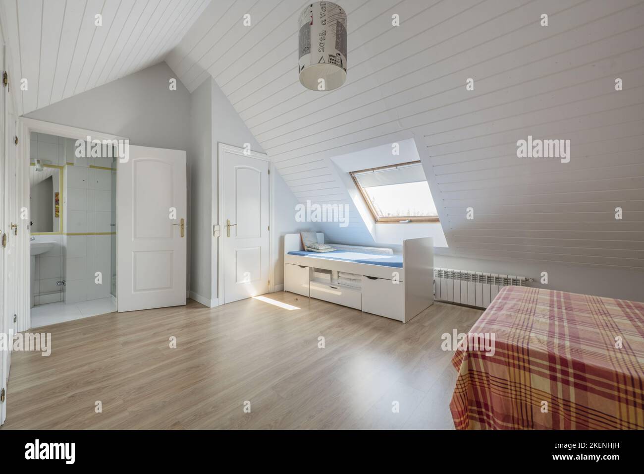 Bedroom with white cabinet doors, bed with striped bedspread, sloping ceilings and youthful bed with drawers, skylight in the ceiling and en-suite toi Stock Photo
