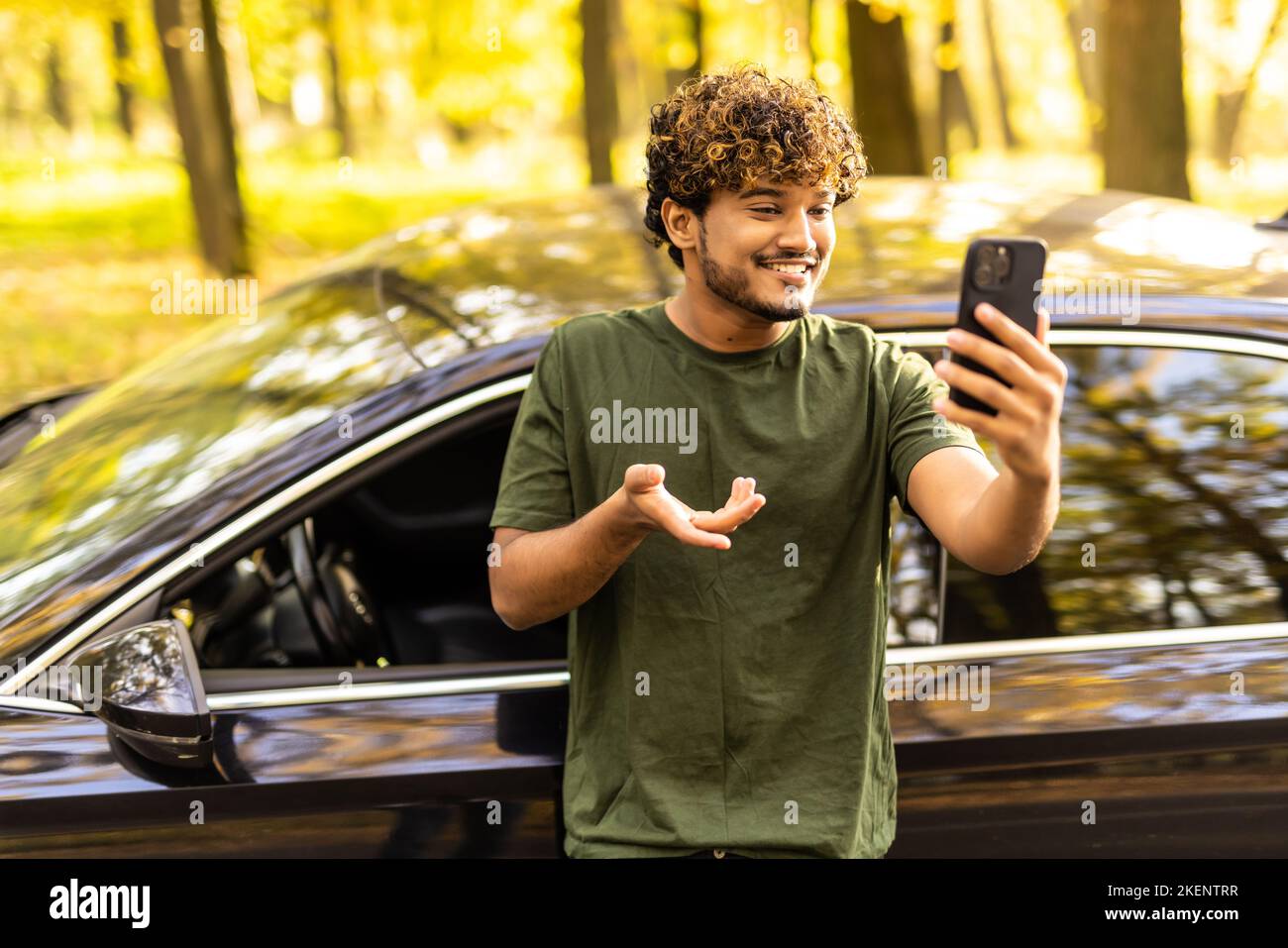 Young indian curly man standing near his car and make video call on the phone Stock Photo
