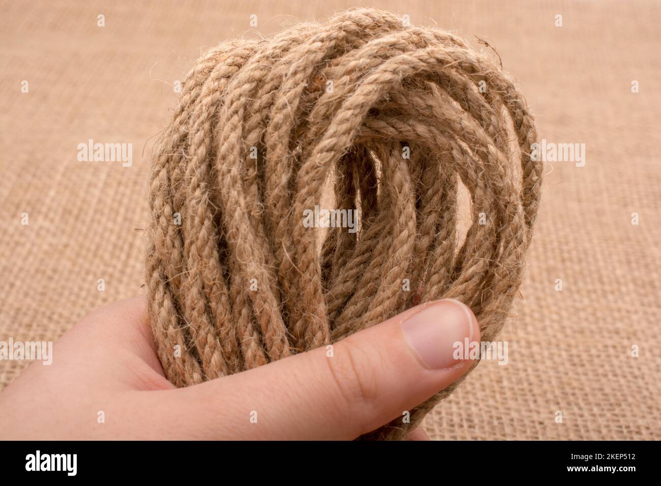 Bundle of linen rope in hand on a brown background Stock Photo - Alamy