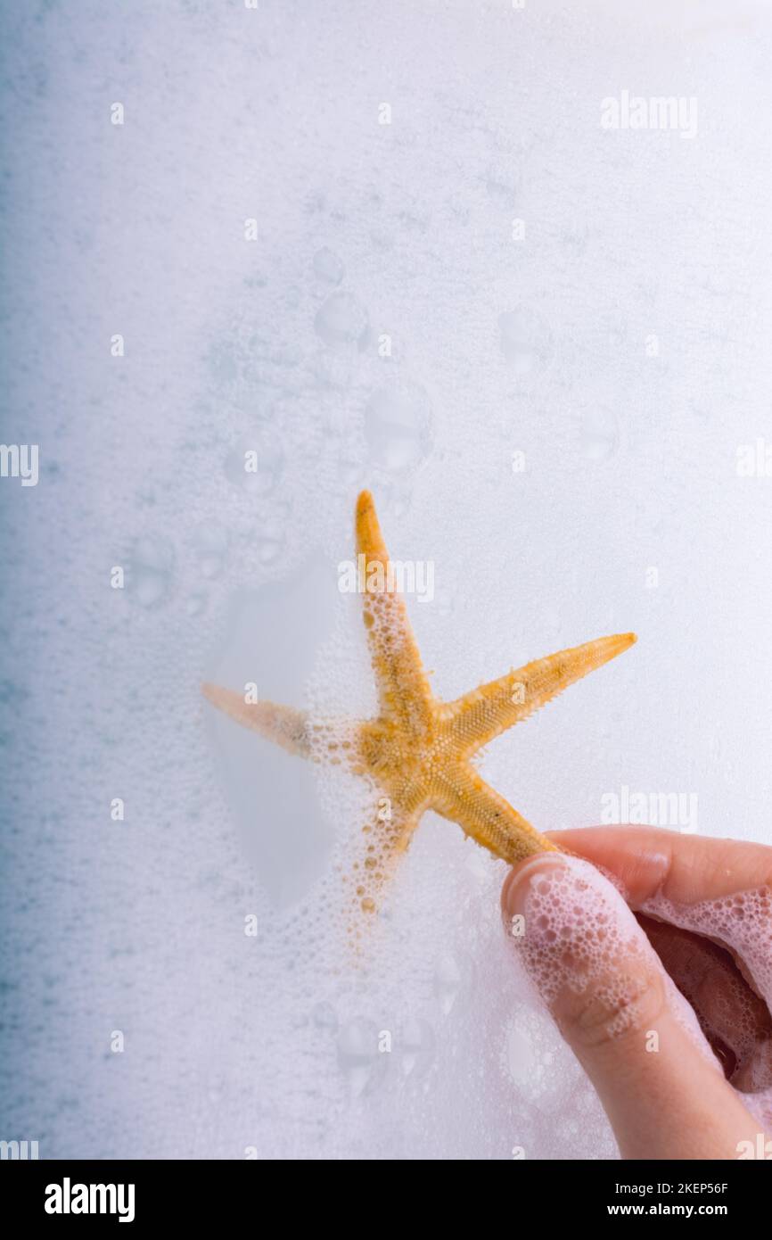 Hand holding starfish in water covered with foam Stock Photo