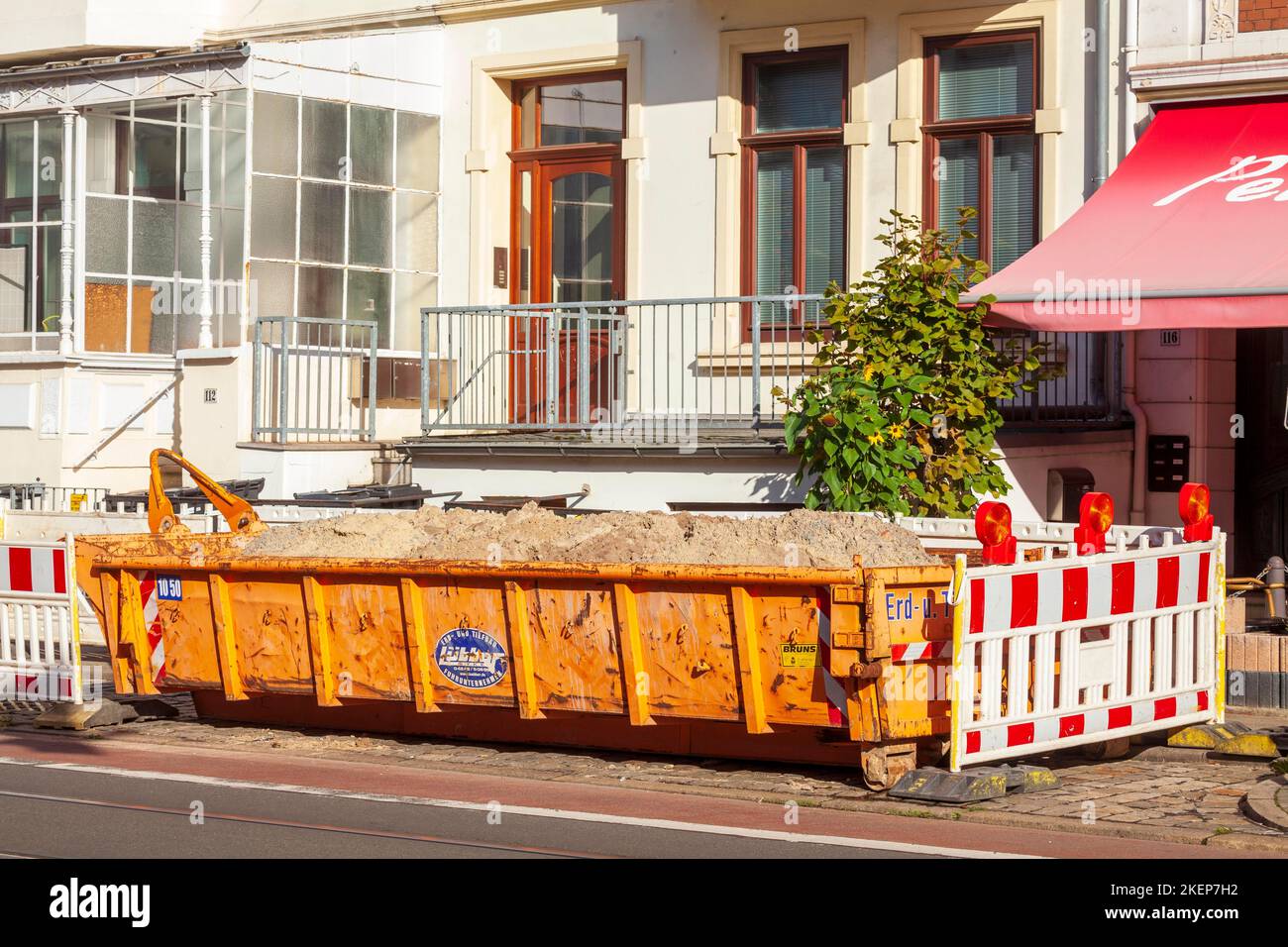 Orange skip for construction waste standing on the road in front of