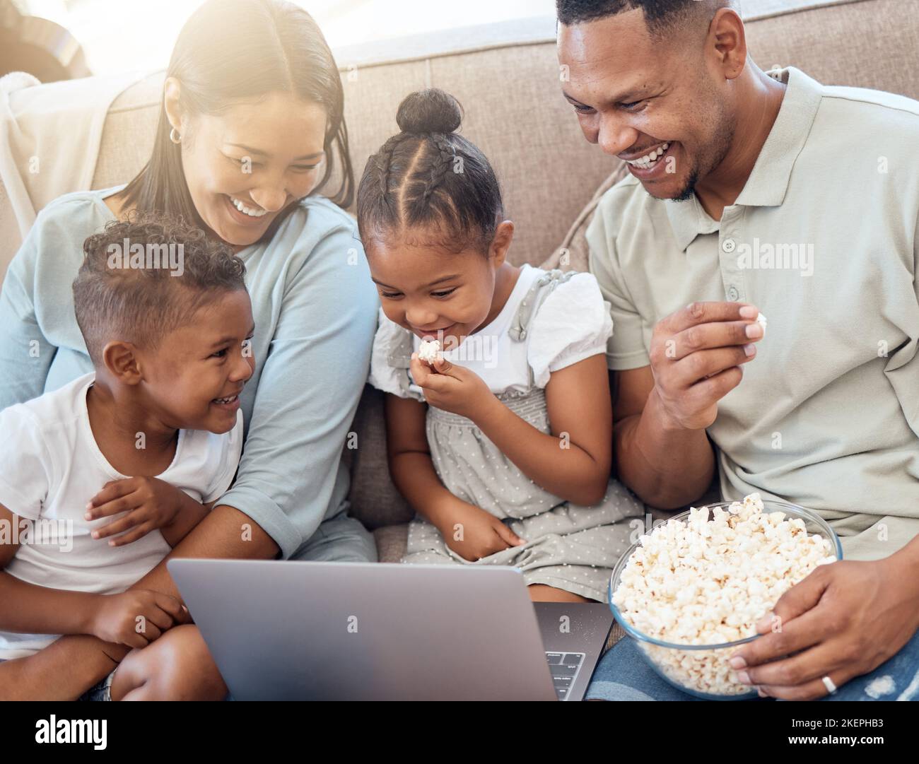 Movie, popcorn and family on sofa with laptop watching, streaming and laughing at comedy. Love, black family and mom and dad with children eating Stock Photo