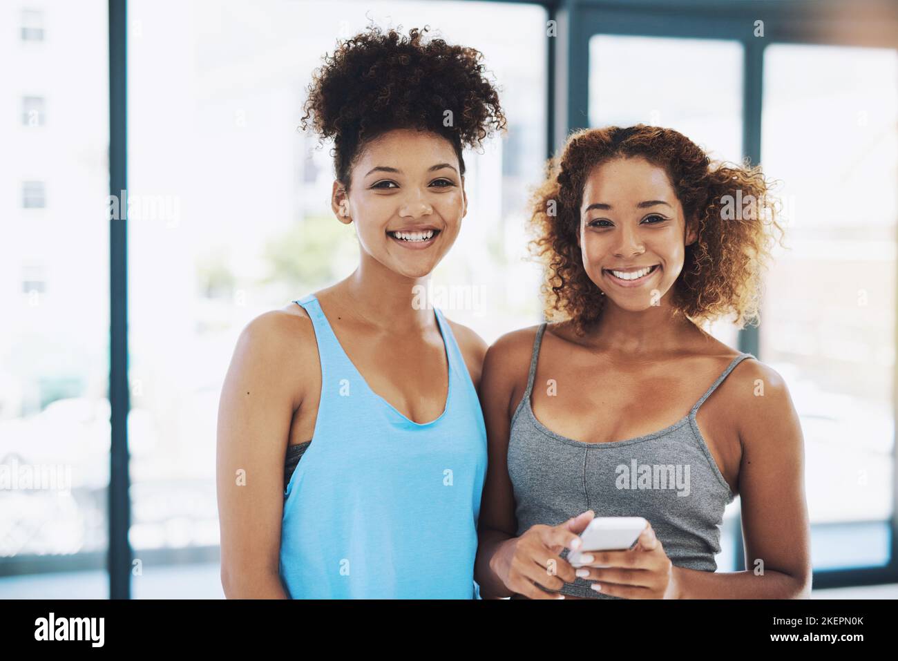 Two besties. Portrait shot of two young fit women using a phone while looking at the camera inside of a studio. Stock Photo