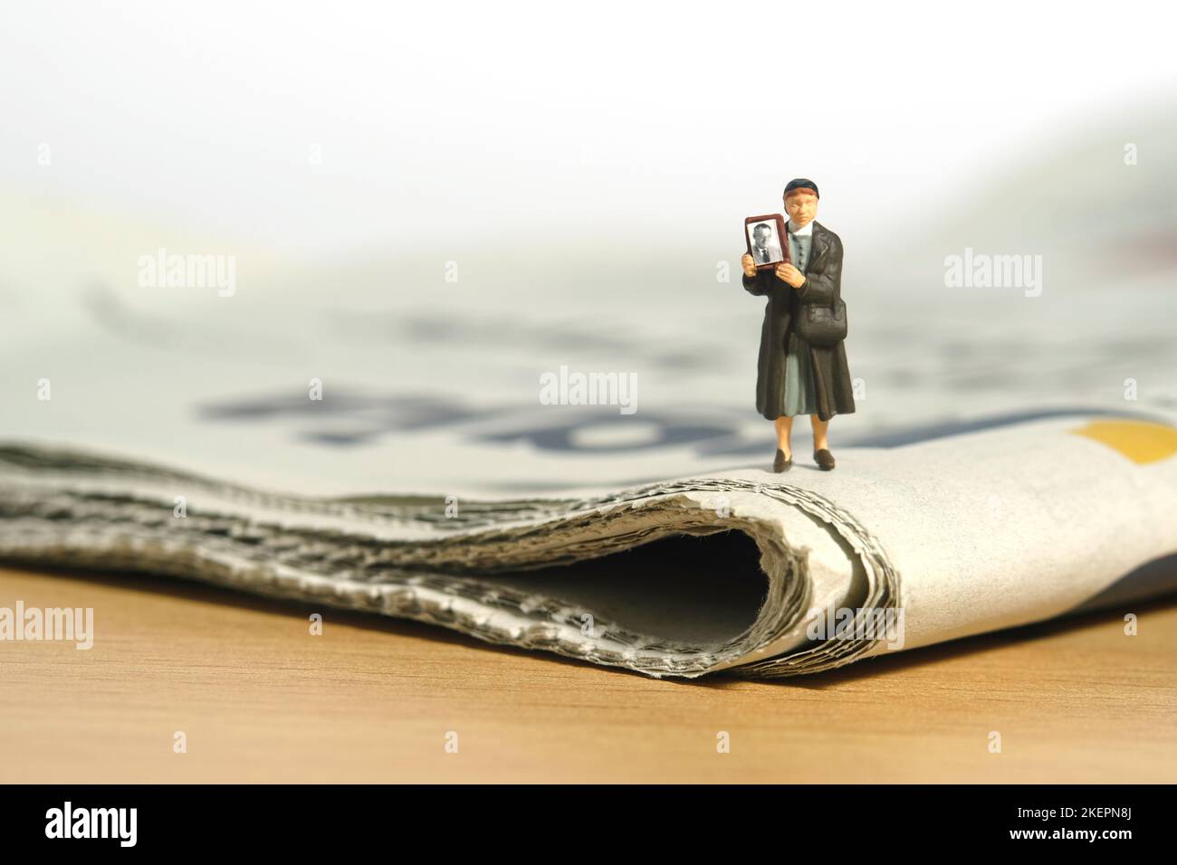 Miniature people toy figure photography. A woman holding photo frame, searching missing person because of war conflict above newspaper. Image photo Stock Photo