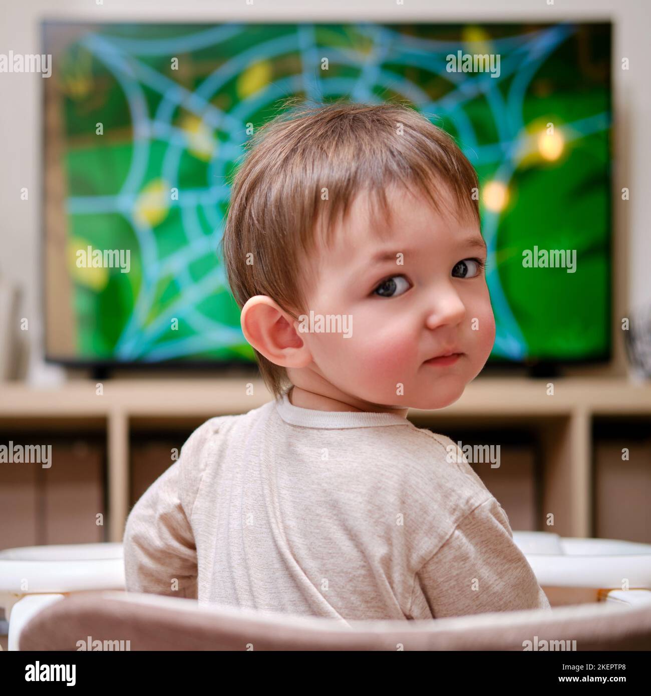 Happy toddler baby boy is watching cartoons on a big TV screen. A child