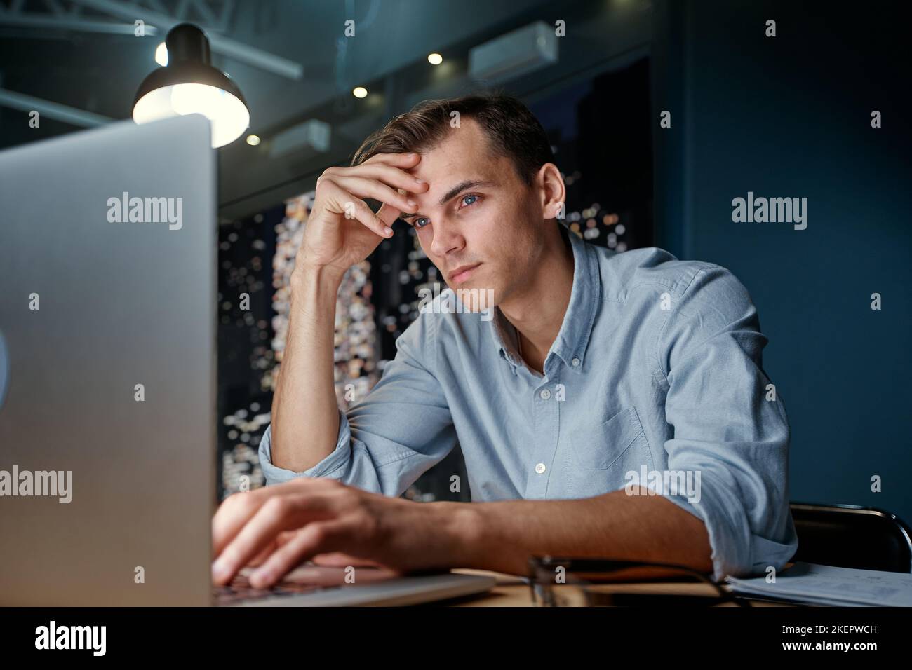 thoughtful young man looking at a laptop screen . Stock Photo