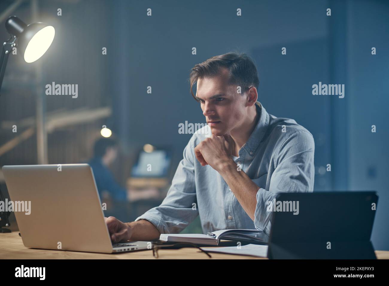 thoughtful businessman using a digital tablet and taking notes in a notebook . Stock Photo
