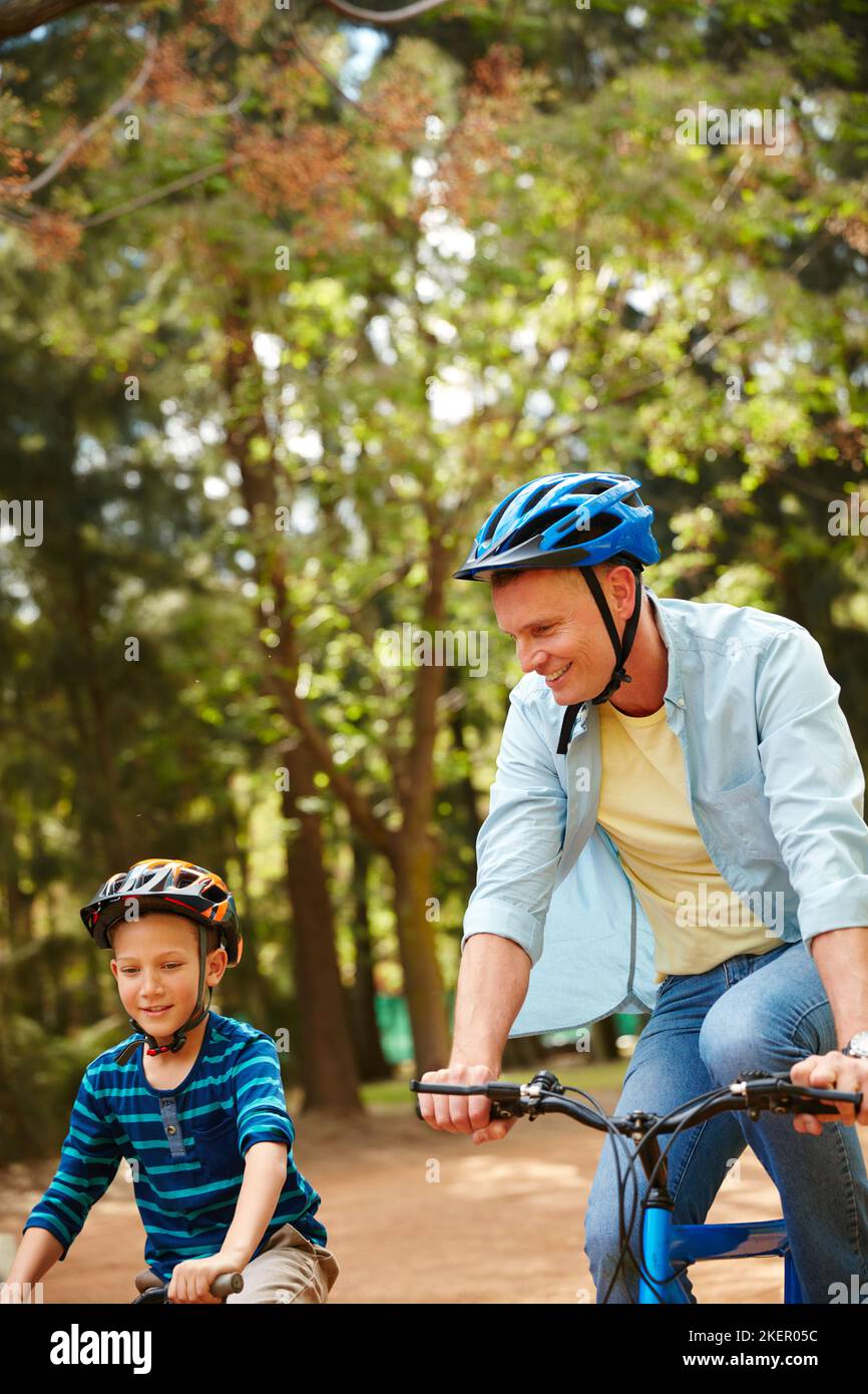 Rolling through the park with dad. a father and his young son riding bicycles through a park. Stock Photo