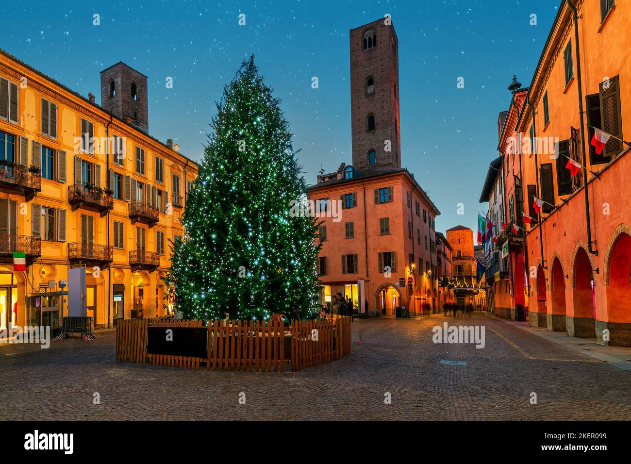 Illuminated Christmas tree on cobblestone town square among old historic buildings in Alba, Piedmont, Northern Italy. Stock Photo