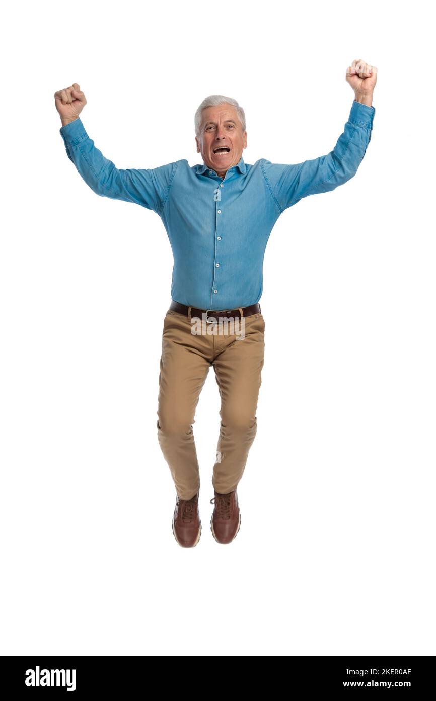 enthusiastic old man in casual outfit with arms above head jumping in the air and laughing while celebrating the winning on white background in studio Stock Photo