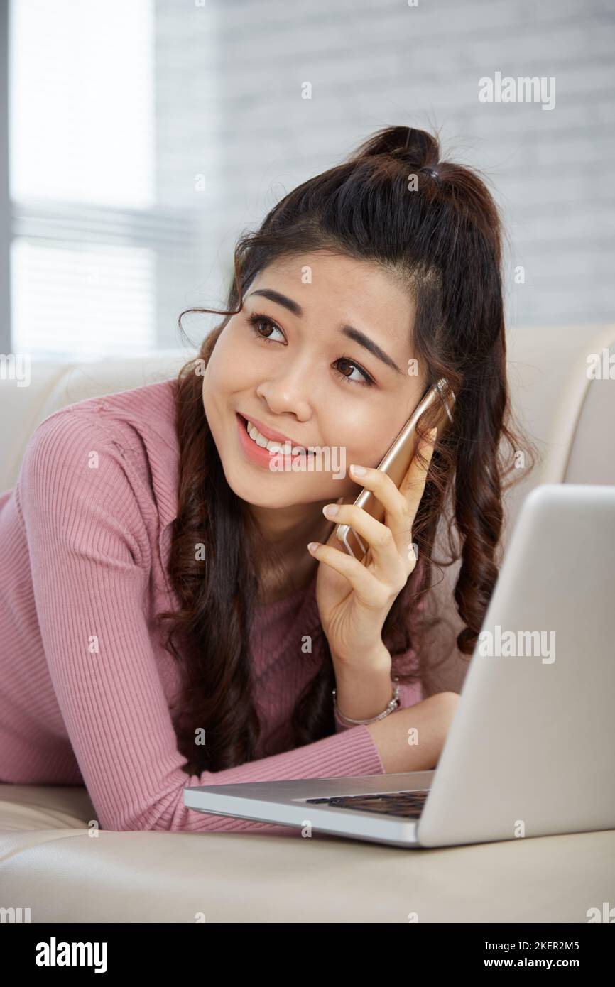 Beautiful young woman lying on sofa and calling on phone to friend Stock Photo