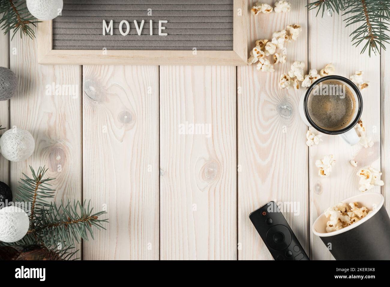 Watching movie film at home on TV with cup of coffee and popcorn, top view. Decorative spruce branches and christmas tree balls. White planking Stock Photo