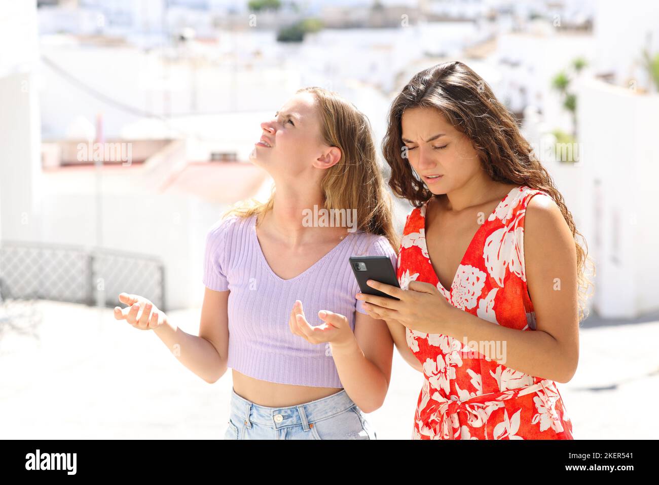 Lost tourists checking smart phone on vacation in a town standing in the street Stock Photo