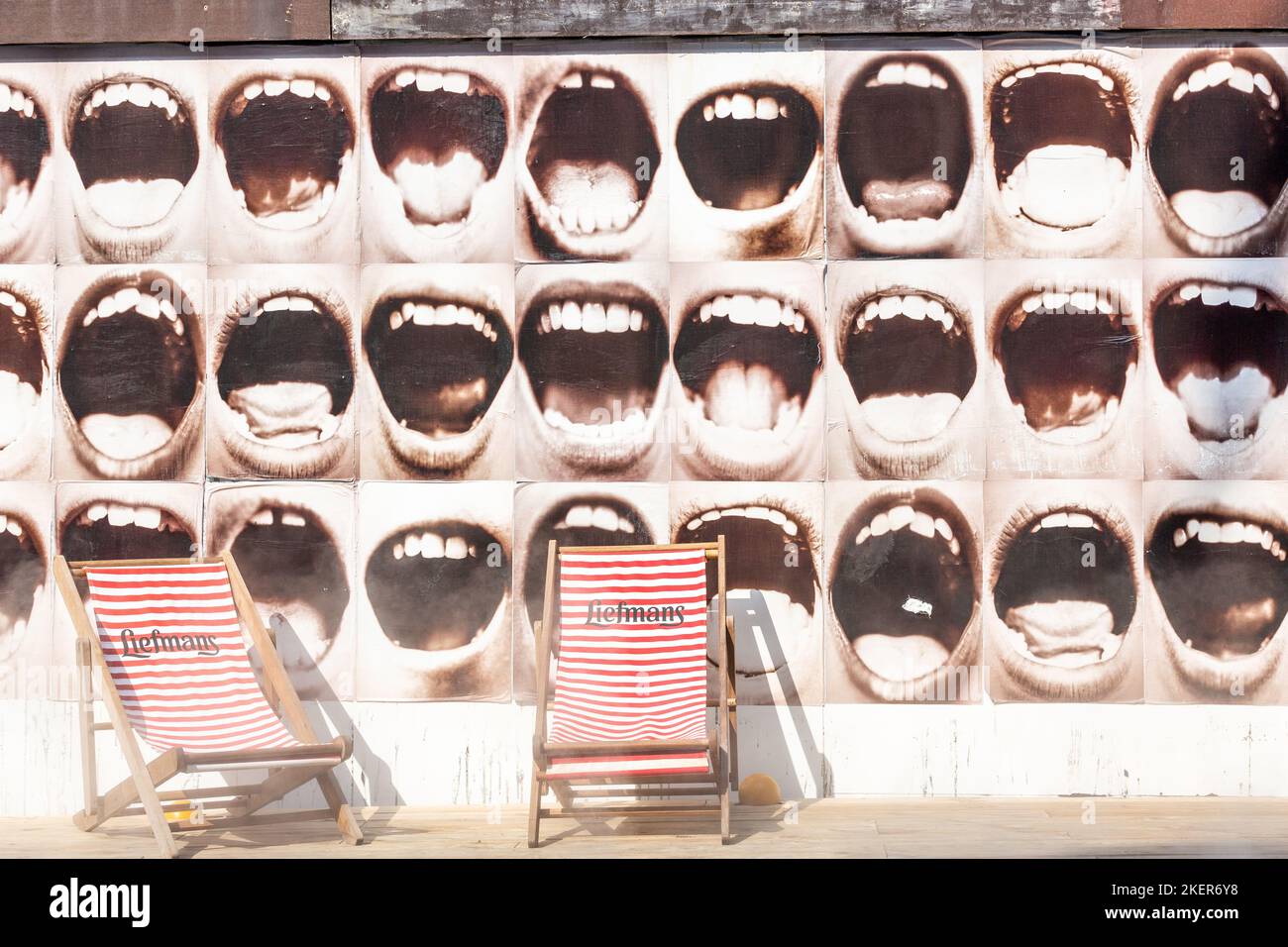 Two deckchairs in front of a wall illustrated with wide open human mouths. Brussels. Stock Photo