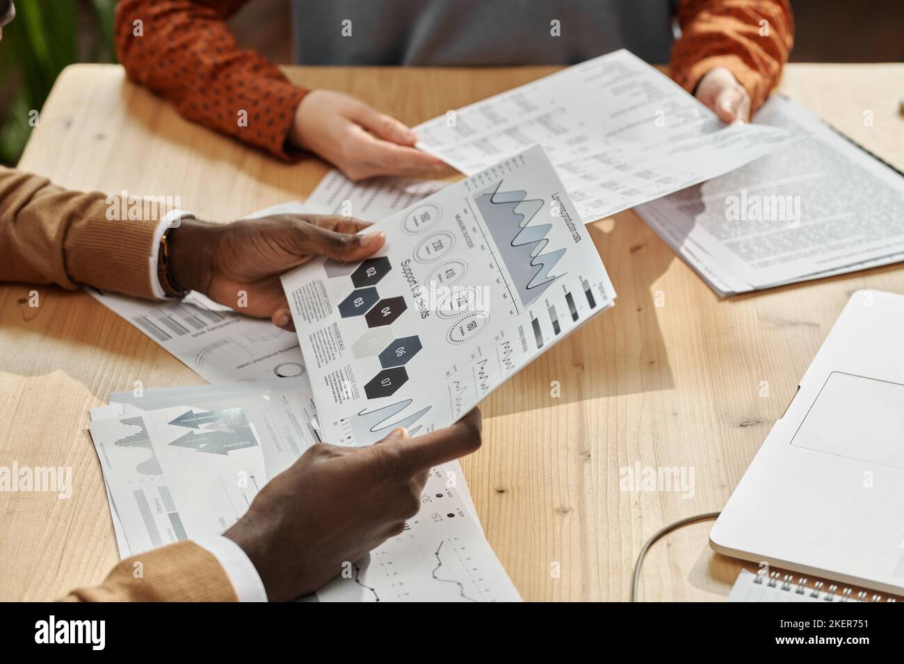 Close-up of colleagues discussing financial graphs together at wooden table at office Stock Photo