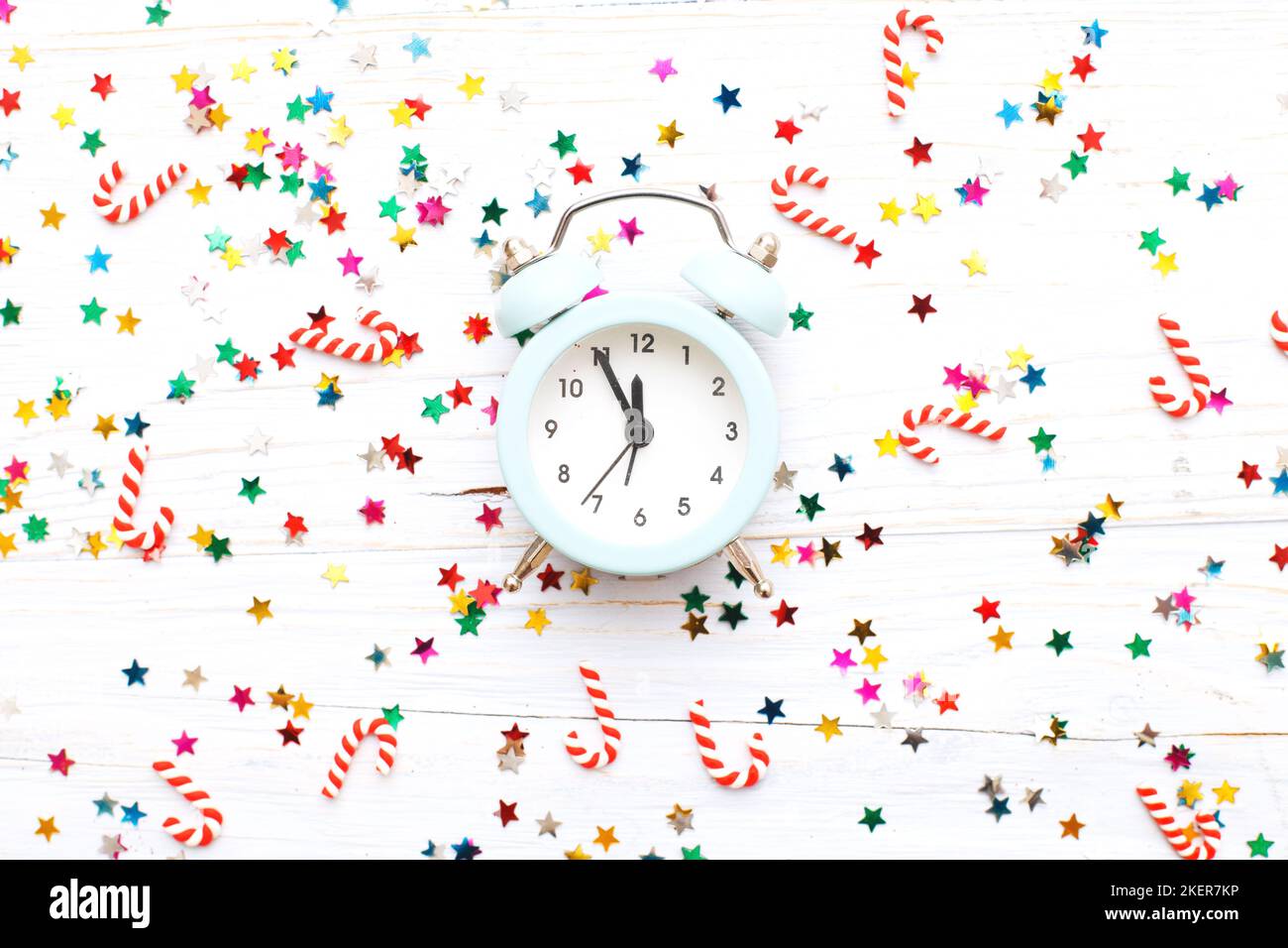 Christmas background with candy canes with the alarm clock and multicolored sequins on blue wooden background. Stock Photo