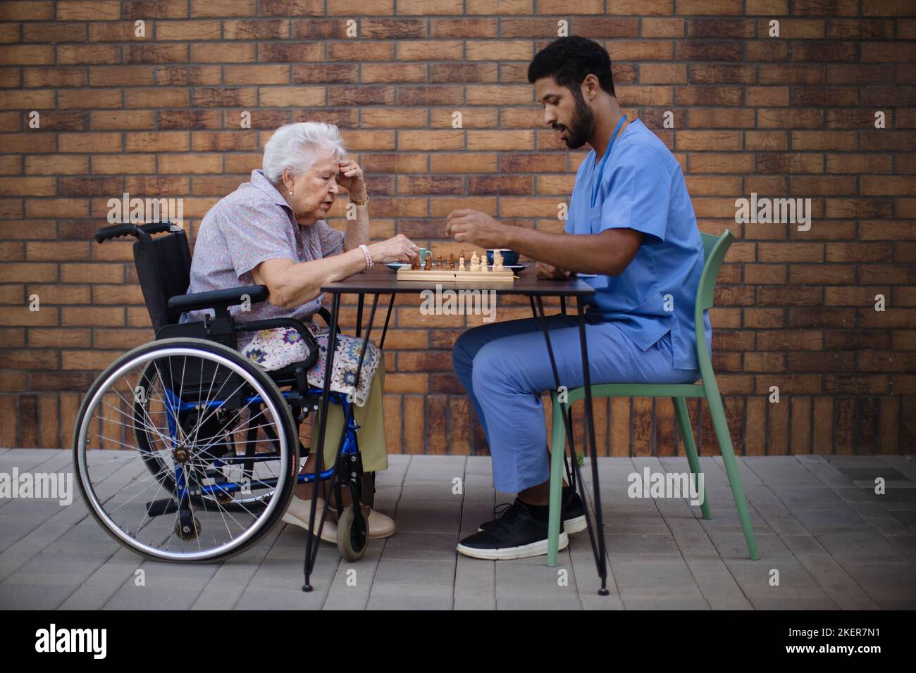 Caregiver playing chess with his client outdoor at cafe. Stock Photo