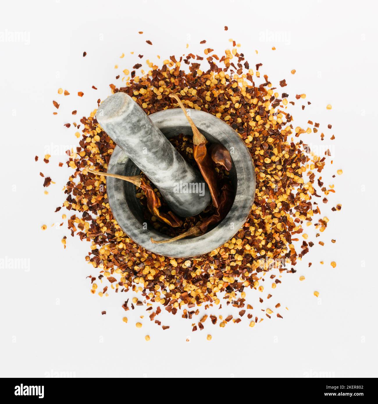 Stone mortar and pestle full of crushed red cayenne pepper, dried chili flakes and seeds