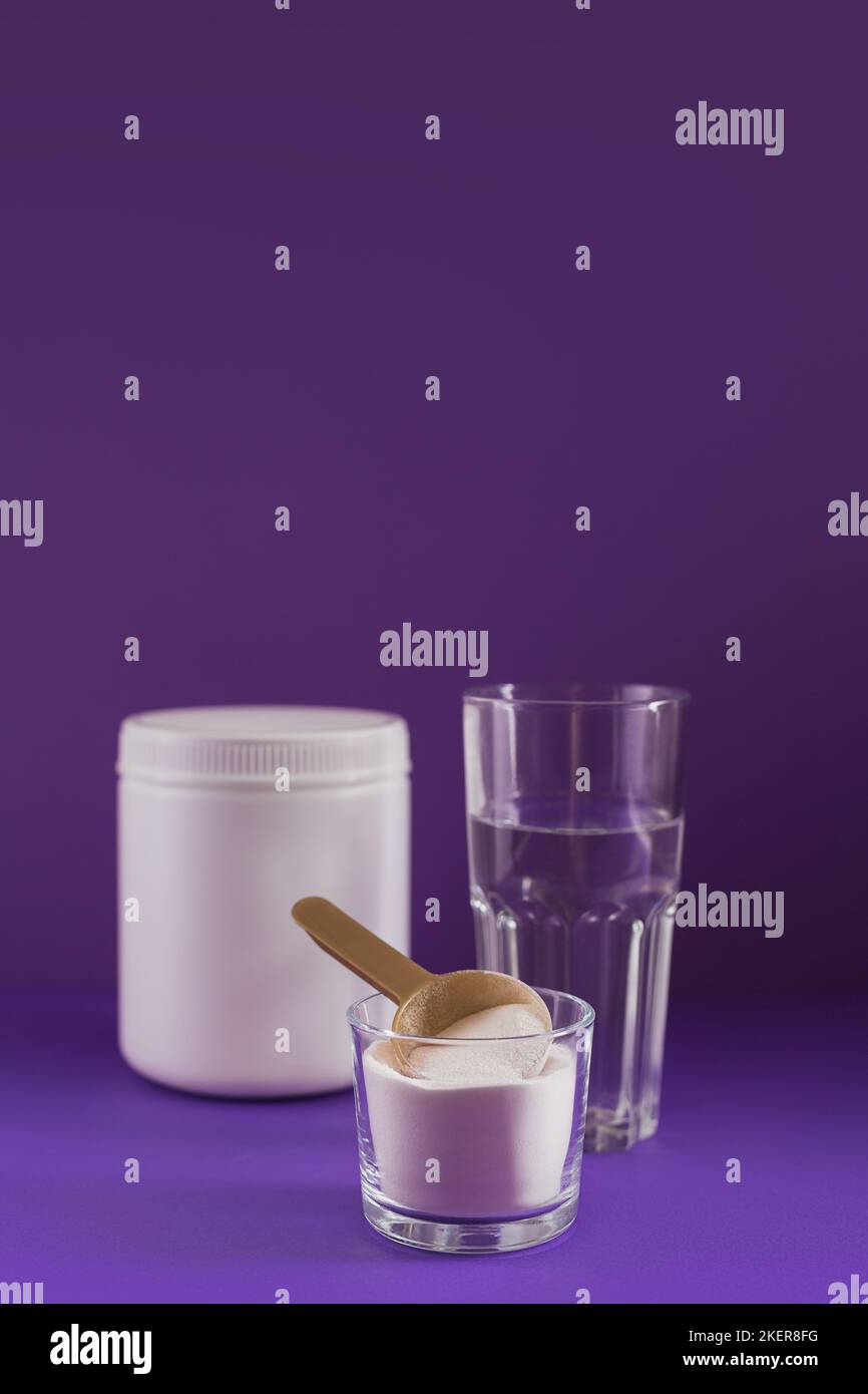 Collagen powder in bowl, glass of water and measure spoon on purple background Stock Photo