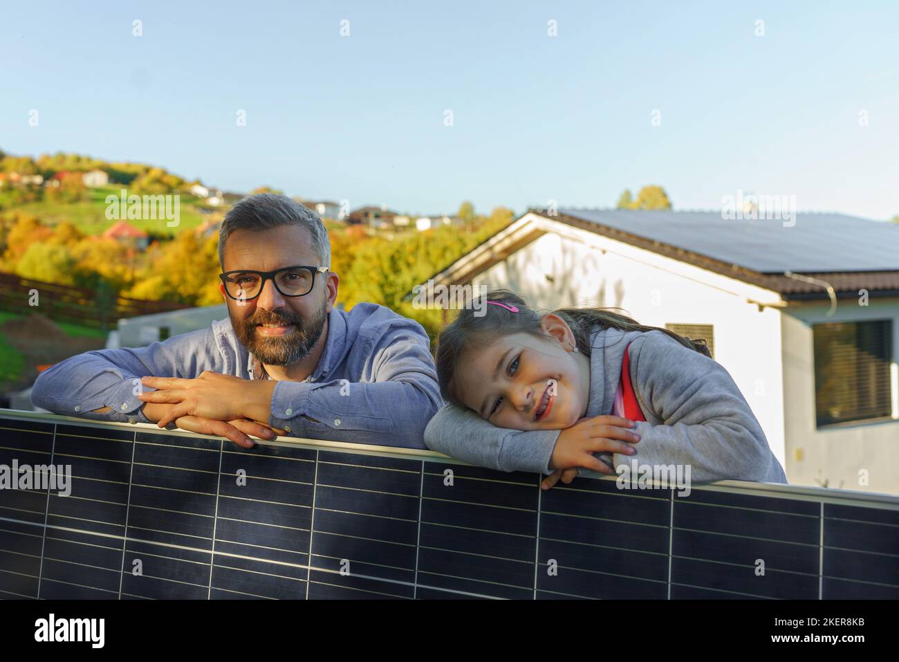 Father with his little daughter near their house with solar panels. Alternative energy, saving resources and sustainable lifestyle concept. Stock Photo