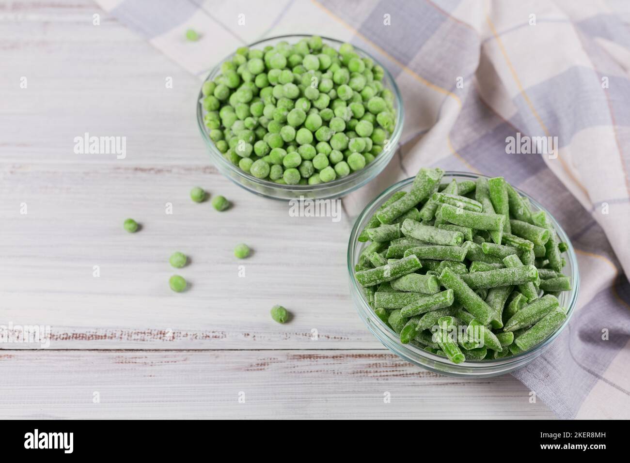 Top view composition with different organic frozen vegetables on a white wooden background. Green beans and peas in a bowl Stock Photo