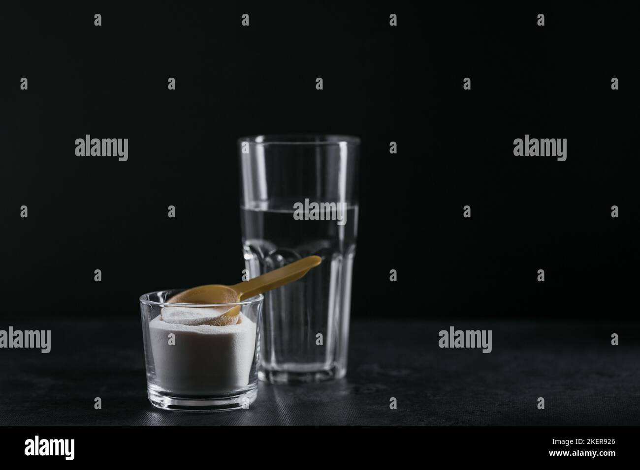 Collagen powder in bowl, glass of water and measure spoon on black background Stock Photo