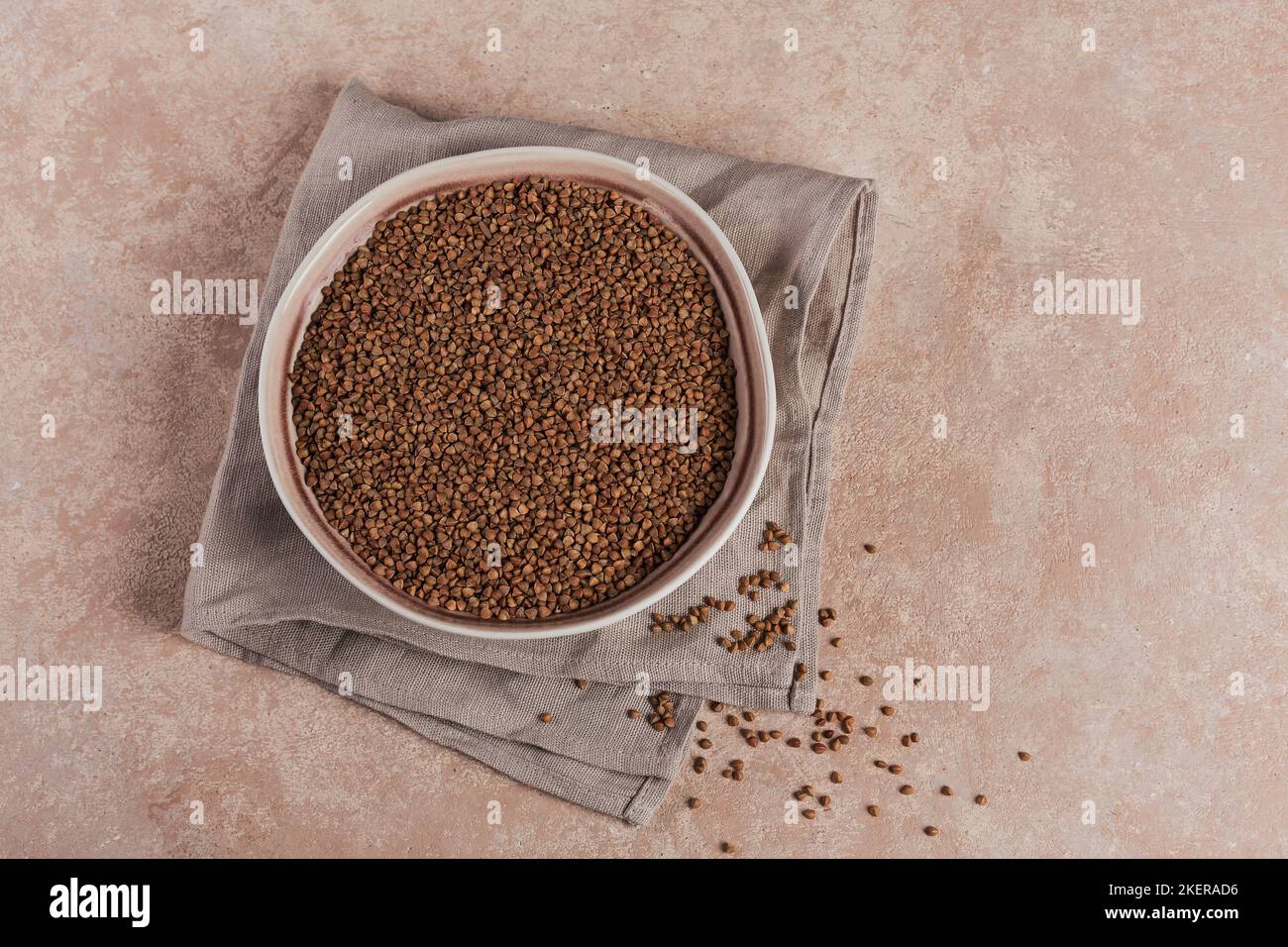 Bowl of dry raw buckwheat groats on a light beige background. Cooking