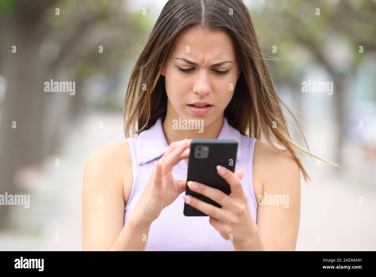 Front view portraif of a worried teen checking smart phone content walking in the street Stock Photo