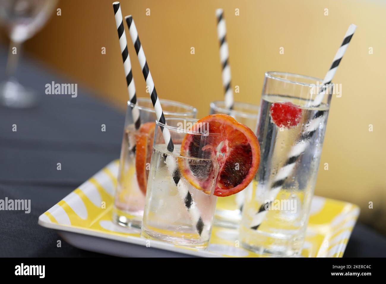 A tray of different tumbler glasses filled with icy cold and clear sparkling water or soda garnished with a slice of blood or red orange and cherries. Stock Photo