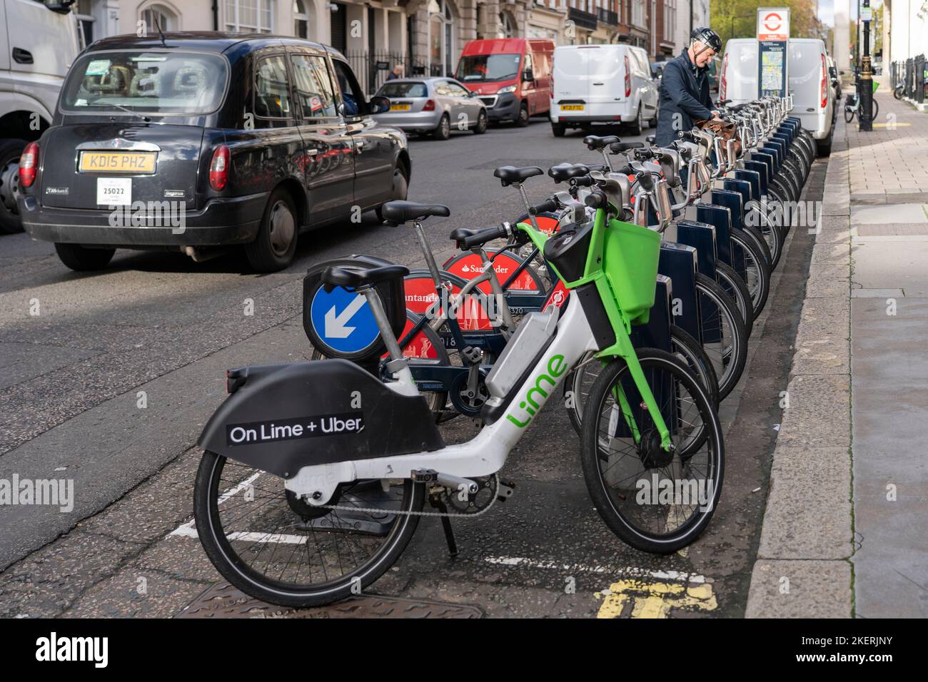 Uber + Lime and Santander sponsored electric bike hire in London. A cyclist picking picking a bicycle as a taxi passes. England Stock Photo