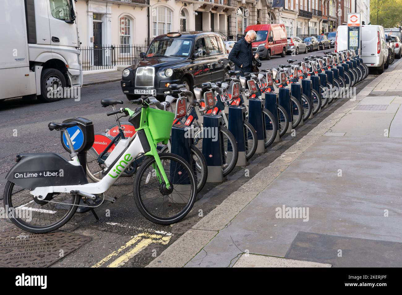 Uber + Lime and Santander sponsored electric bike hire in London. A cyclist picking picking a bicycle as a taxi passes. England Stock Photo
