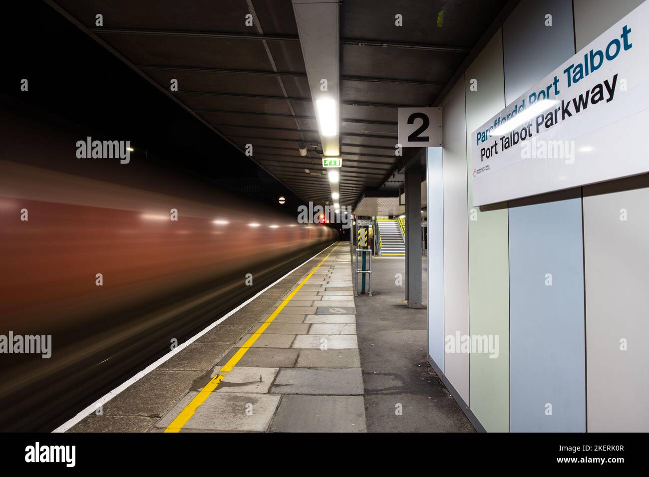 A freight train passing through Port Talbot Parkway Railway Station at night. Stock Photo