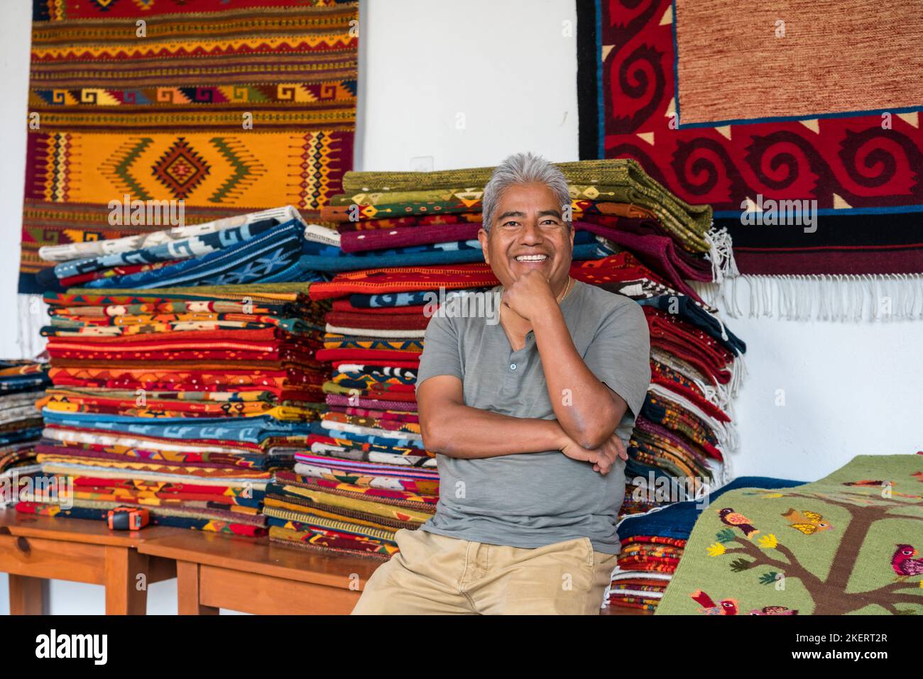 Master weaver Jeronimo Vasquez G. with woolen rugs in the family weaving business in Teotitlan, Oaxaca, Mexico.  The yarn is dyed with all natural dye Stock Photo