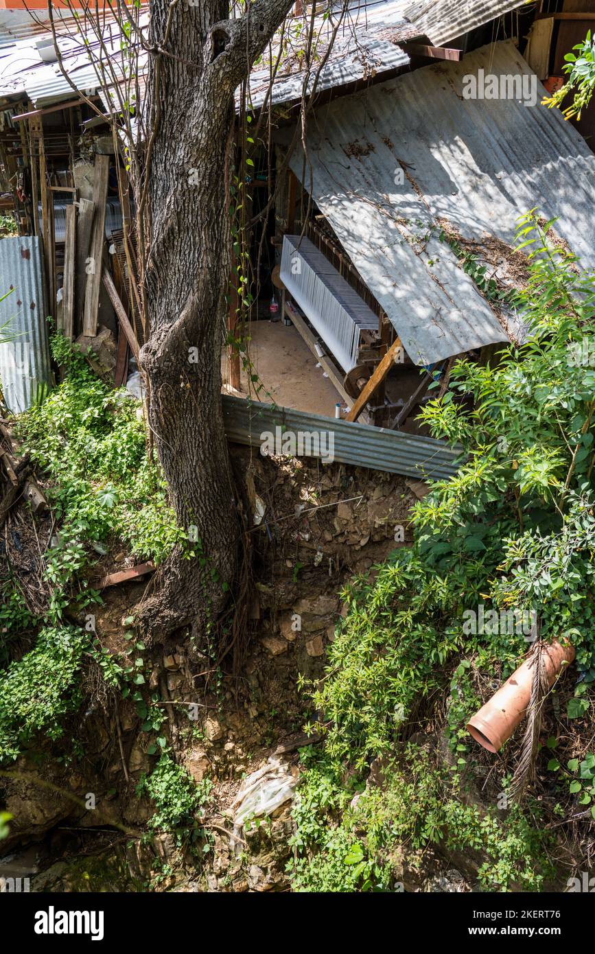A home-based weaving shop precariously perched on the side of a deep ravine in Oaxaca, Mexico.  The large foot-treadle loom is just visible under the Stock Photo