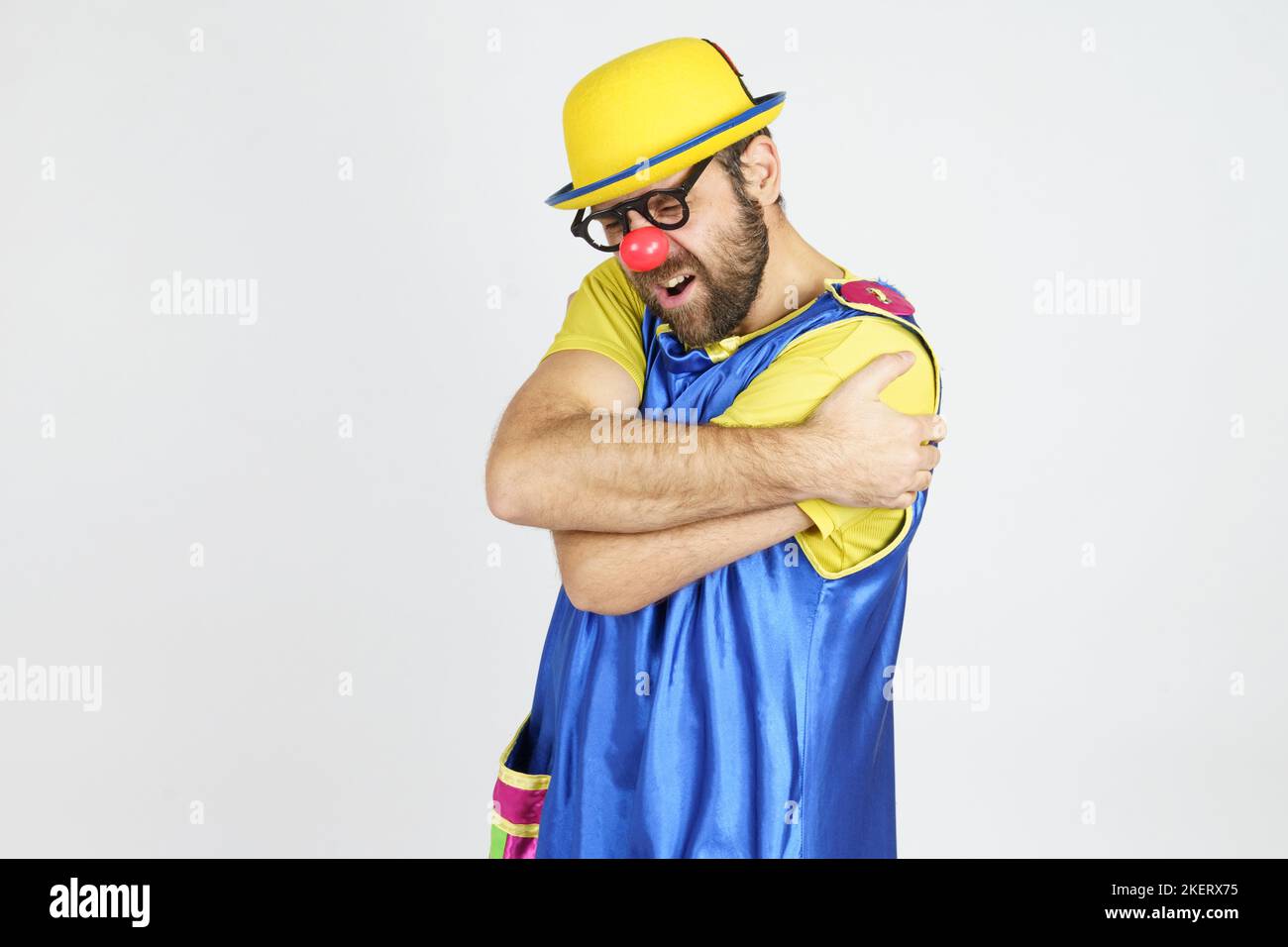 Holiday concept. Clown in a bright blue and yellow suit hugs himself ...