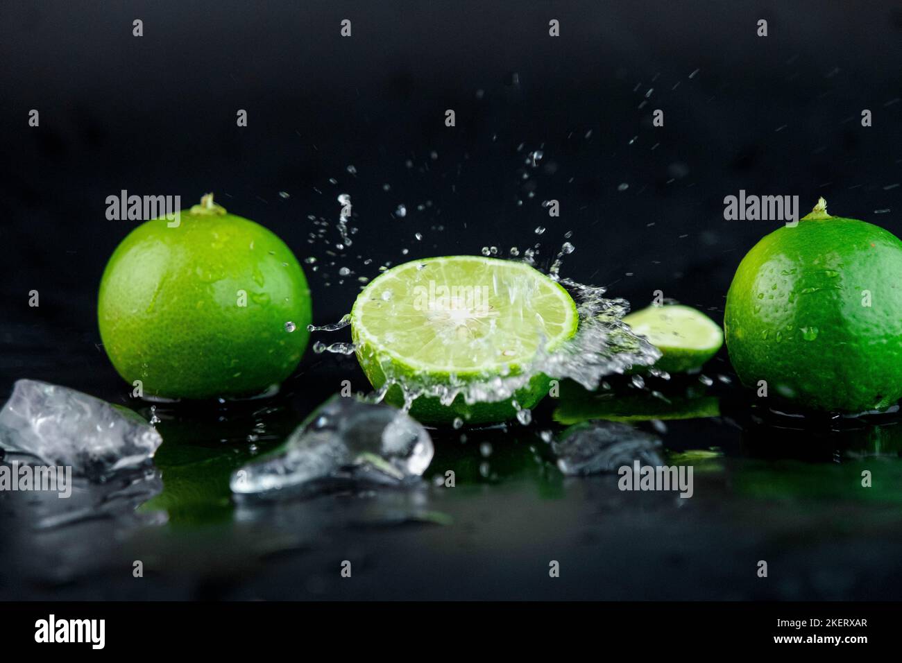 Water drops on lemon slices and splash with ice cubes on table on black background. selective focus. Stock Photo