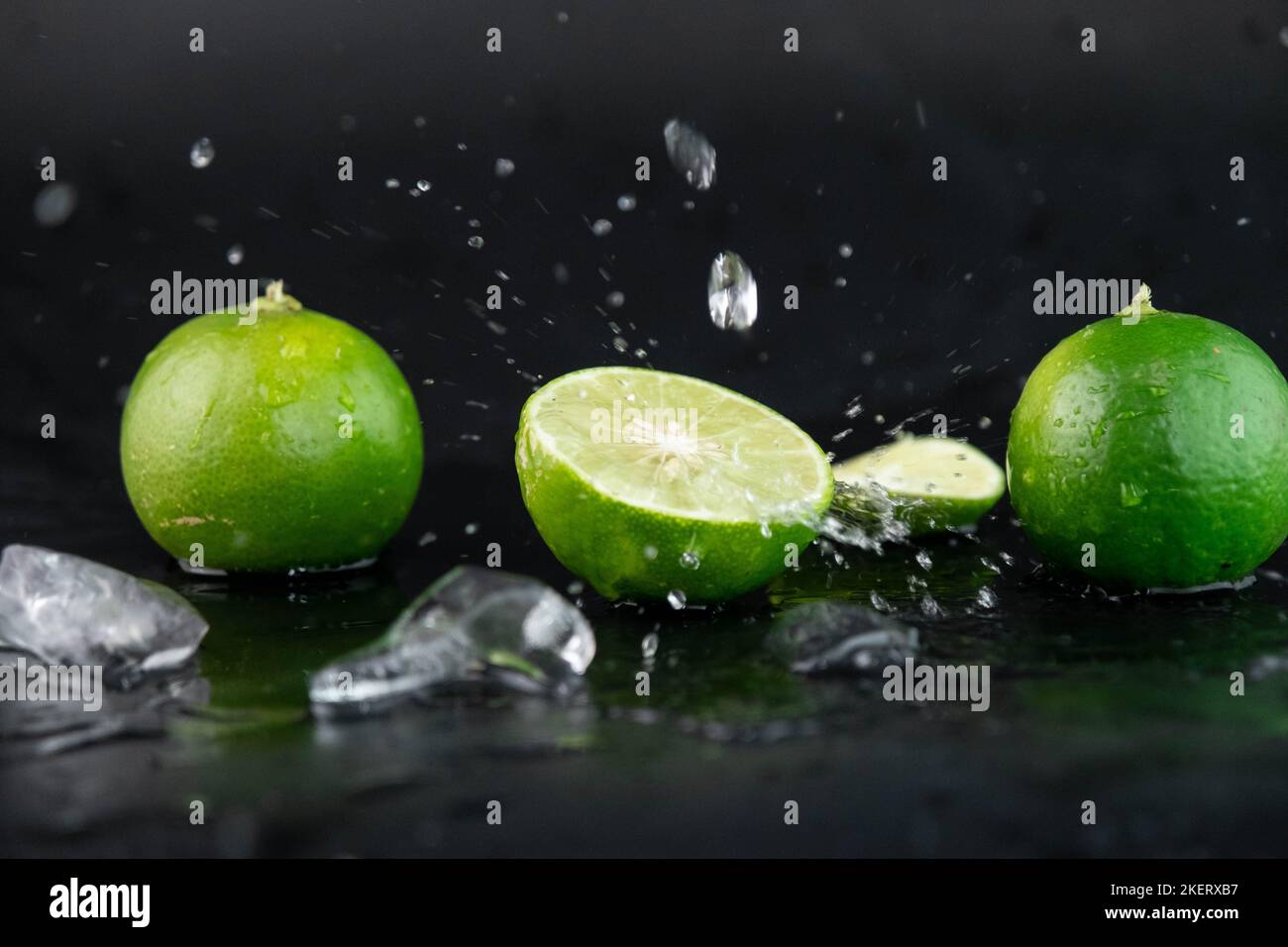 Water drops on lemon slices and splash with ice cubes on table on black background. selective focus. Stock Photo